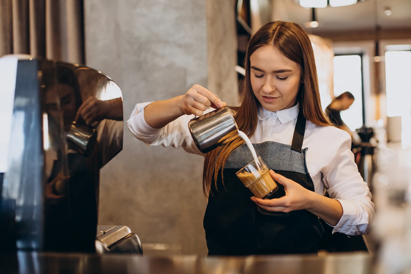 Barista carefully pouring milk while preparing a drink in a cafe