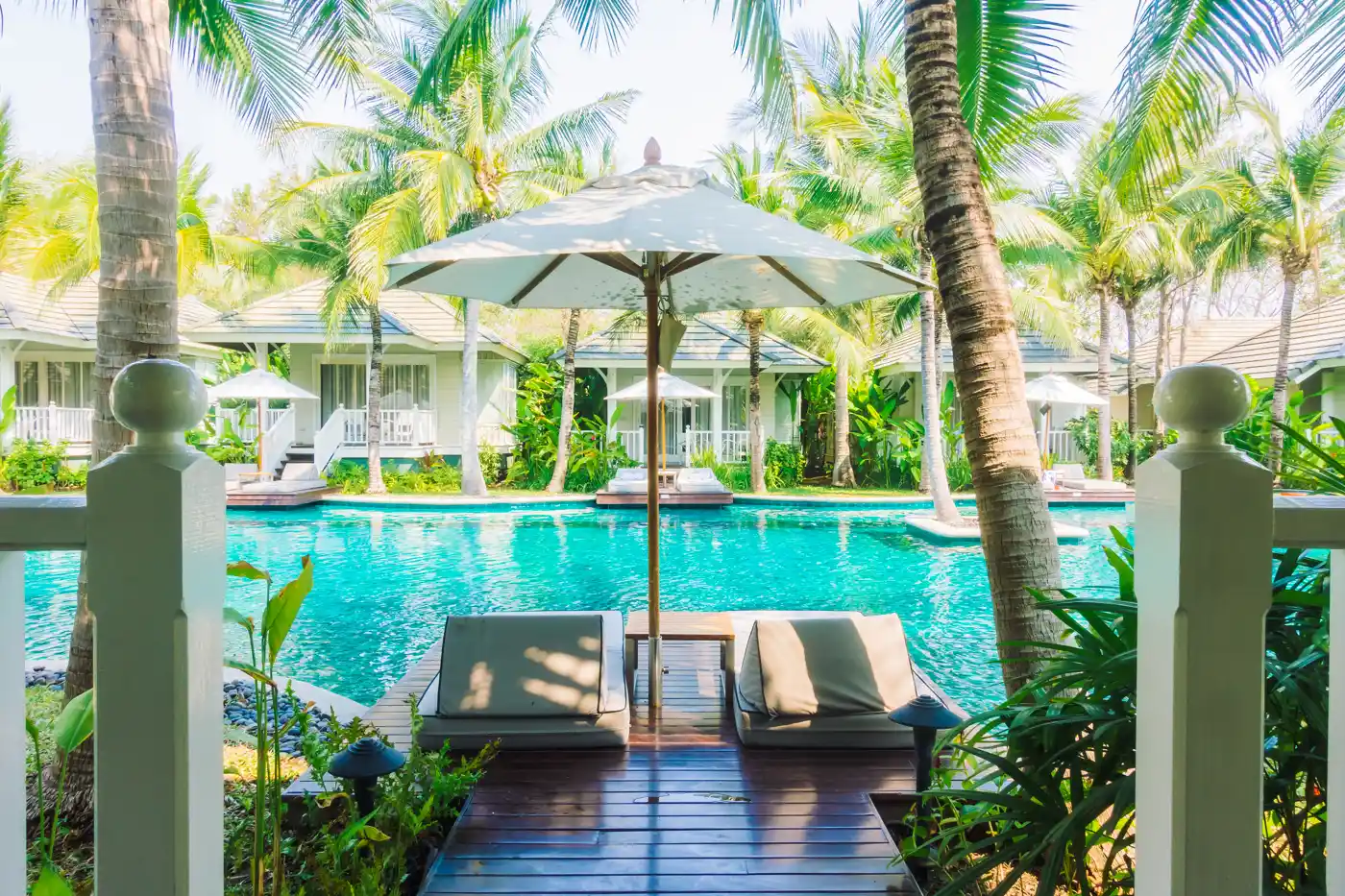 Tropical resort pool surrounded by palms and shaded loungers