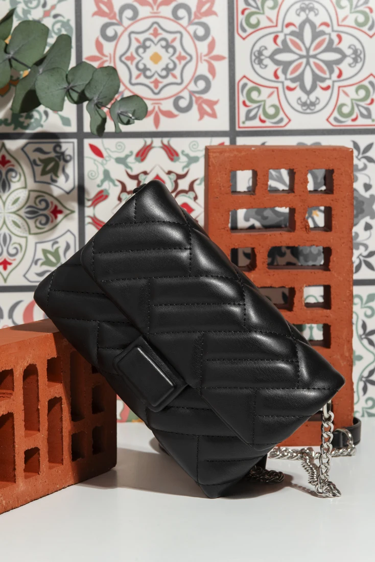Black quilted handbag displayed against decorative tiles